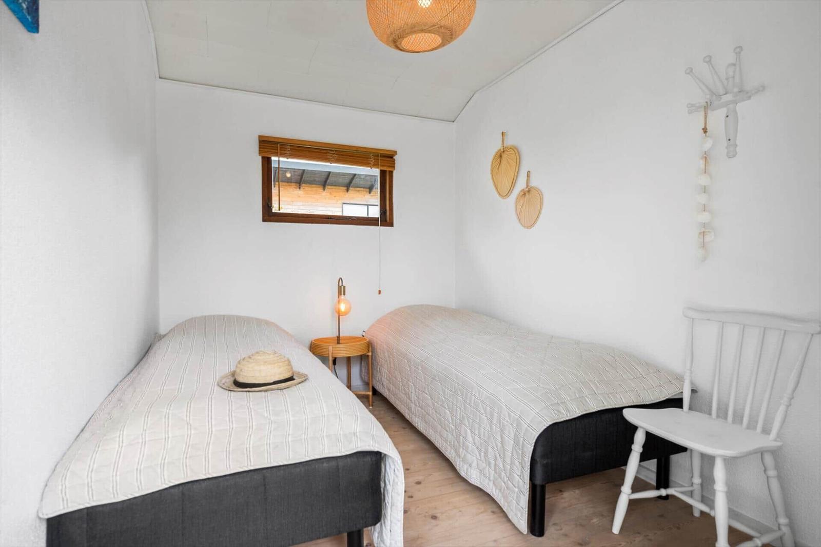 Zwei Betten, ein Fenster, eine Lampe und eine weiße Stuhllehne.
