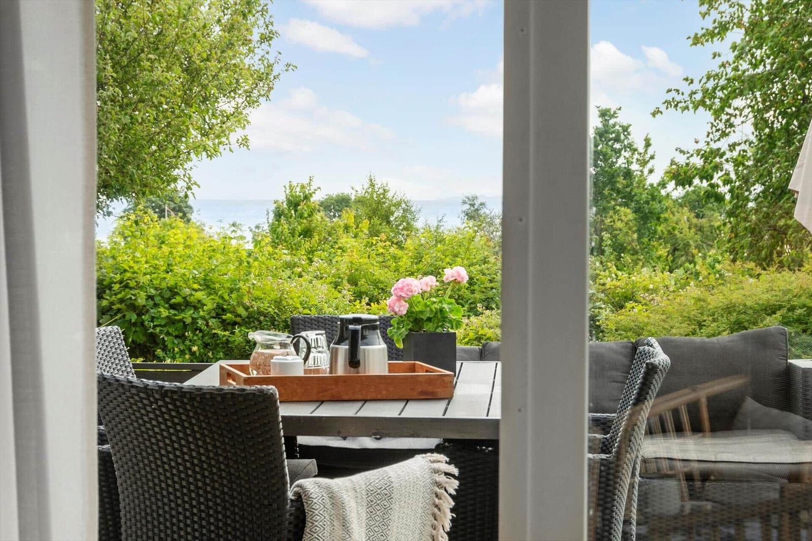 Terrasse mit Tisch, Stühlen und Blick auf Grünflächen und Wasser.