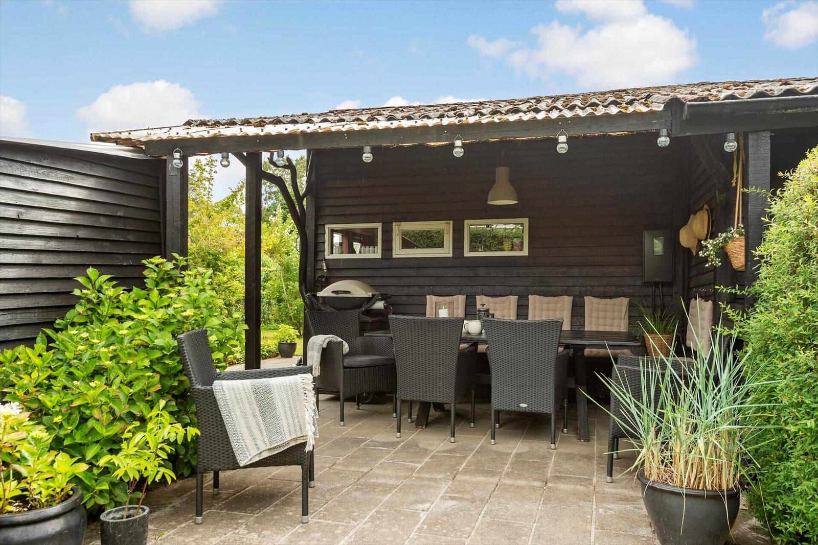 Terrasse mit Sitzgruppe, Grill und Pflanzen unter einem Dach.