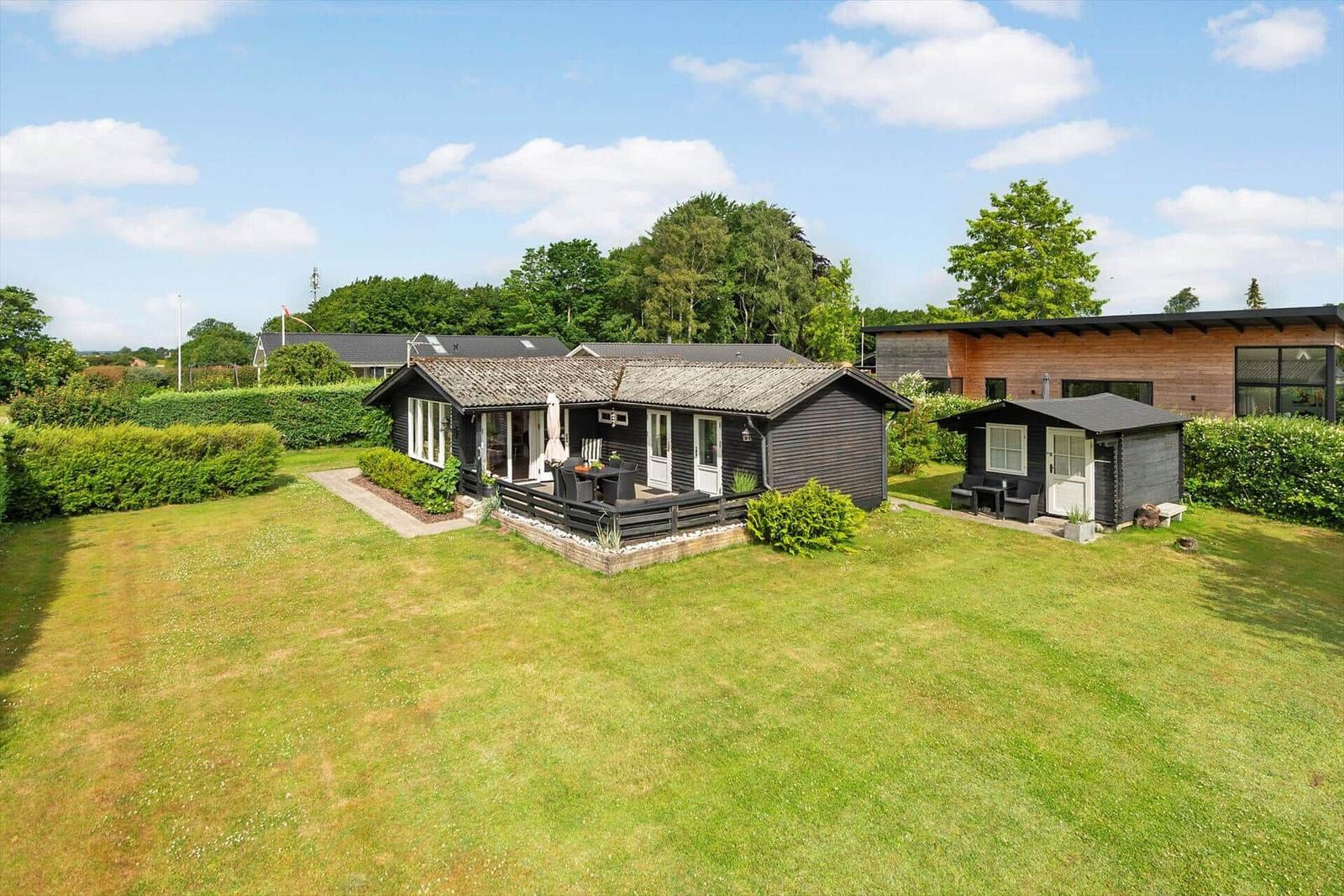 Holzhäuser mit Terrasse und Garten. Umgeben von Bäumen und Grünflächen.