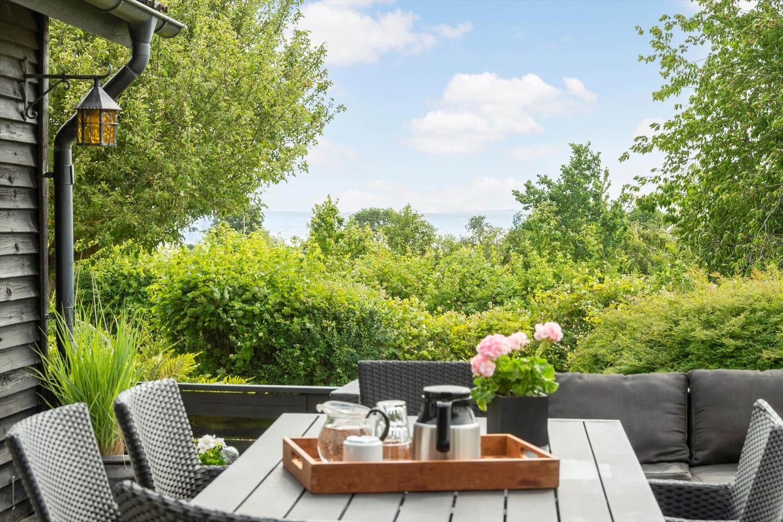 Terrasse mit Tisch, Stühlen und Aussicht auf Grün und Meer.