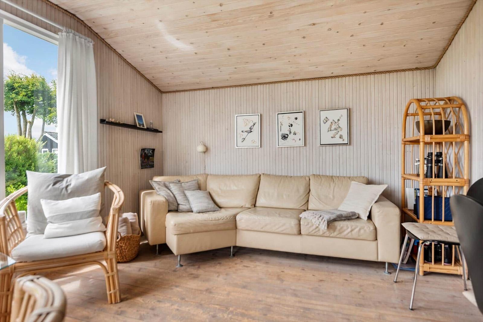 Wohnzimmer mit hellen Wänden, Holzboden und großem Sofa. Fenster mit Blick auf Garten.