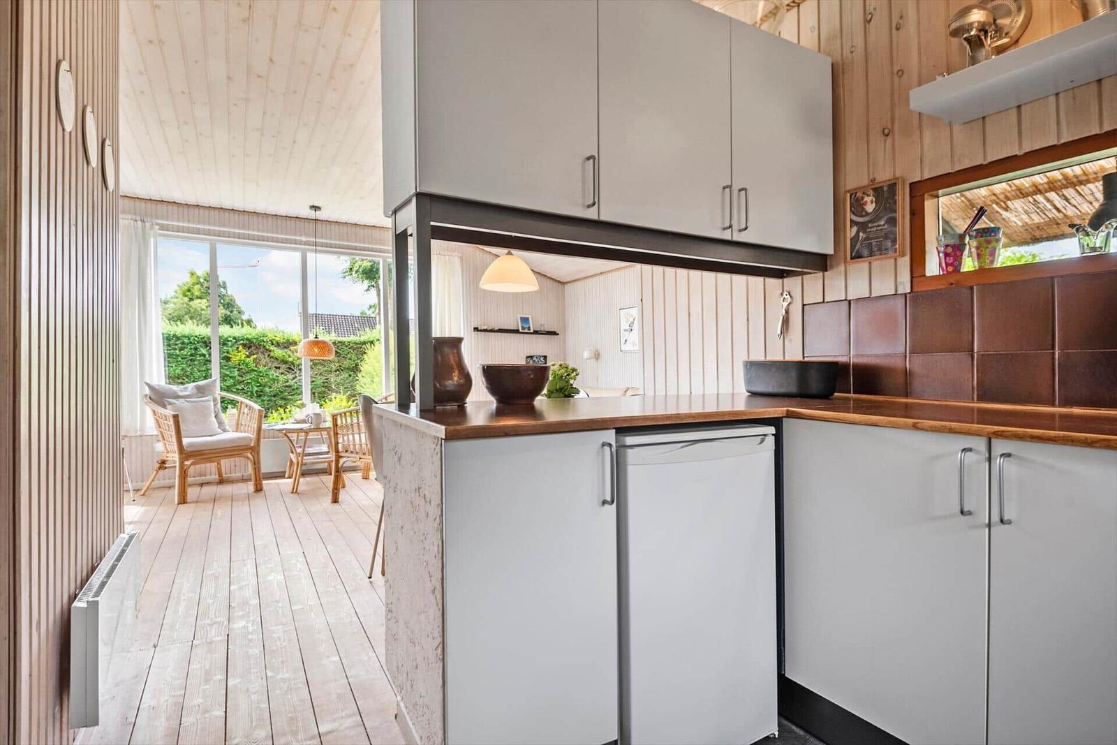 Küche mit Holzoberfläche und integriertem Kühlschrank. Blick in Wohnbereich mit Sitzgelegenheit.