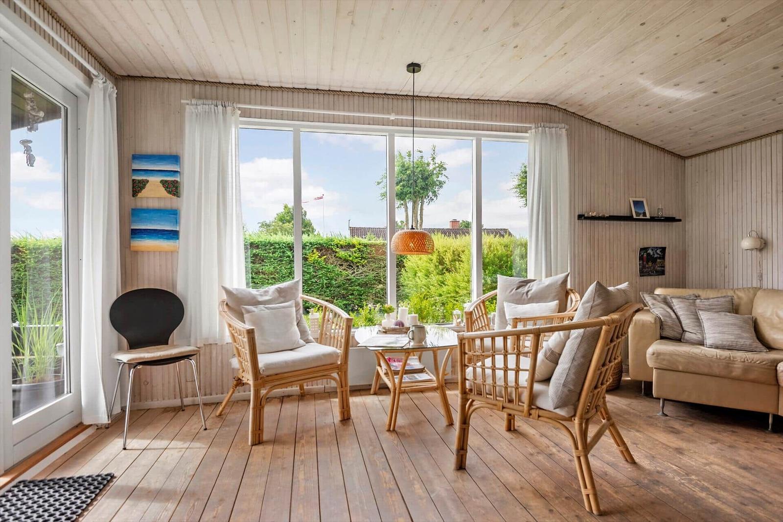 Wohnzimmer mit Holzboden, Sitzgruppe und großem Fenster zur Außenterrasse.
