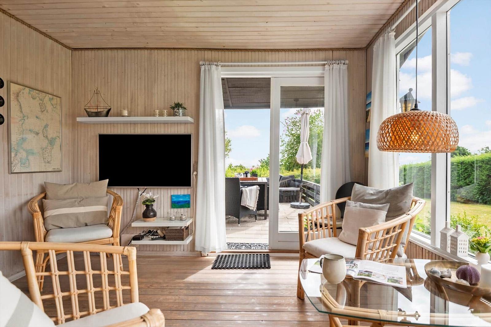 Wohnzimmer mit Rattanmöbeln, Fernseher und Blick auf Terrasse.
