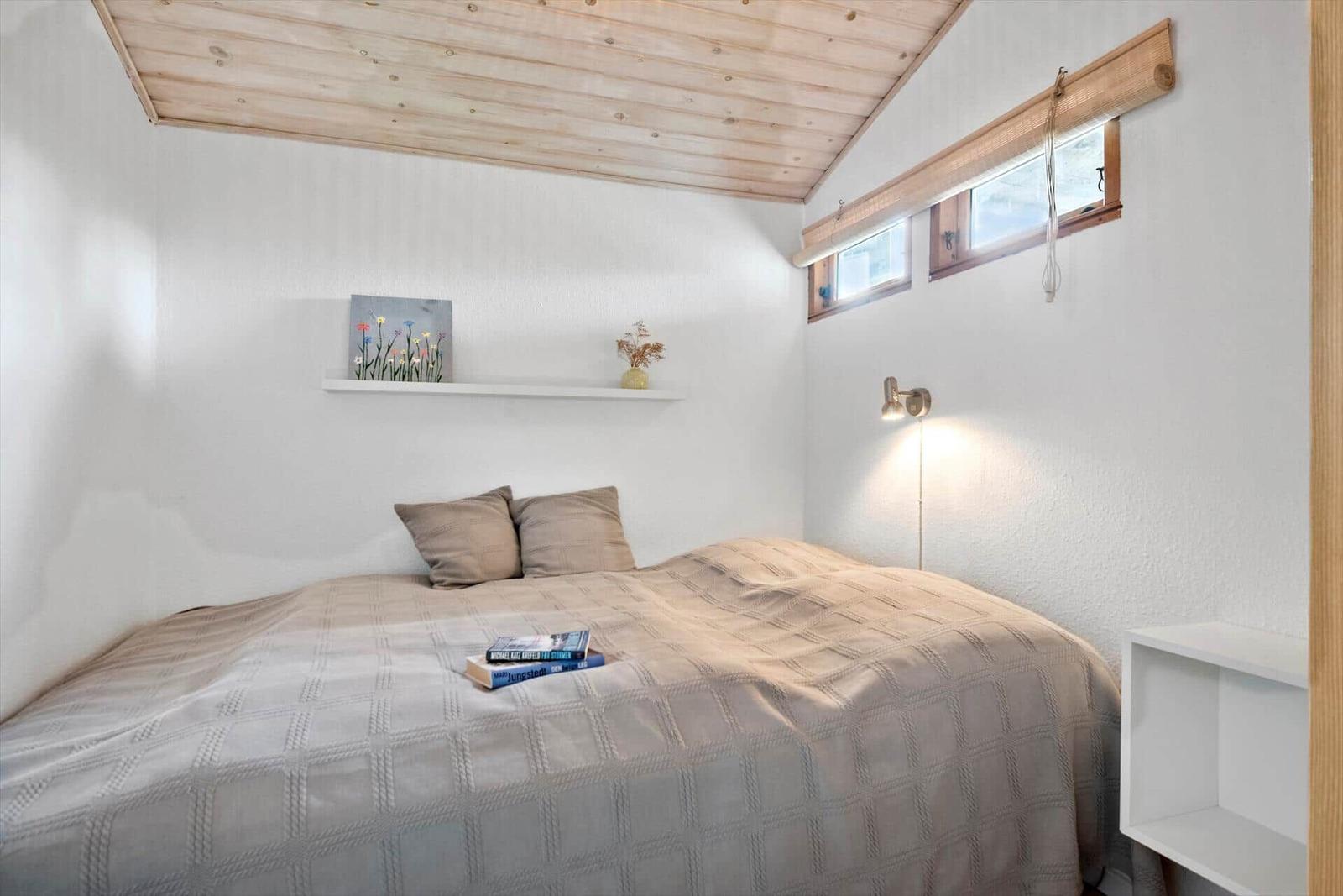 Schlafzimmer mit Bett, Wandregal, Fenster und Deckenbalken.
