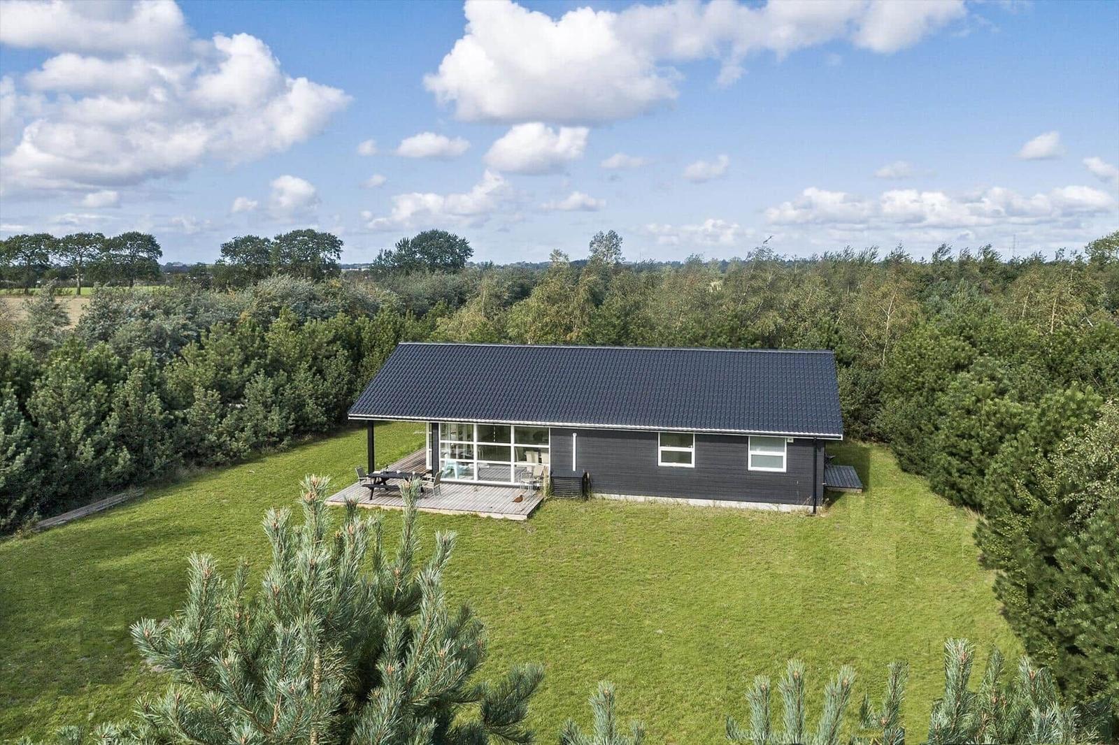 Ein modernes Haus mit Terrasse steht auf einer grünen Wiese umgeben von Bäumen.