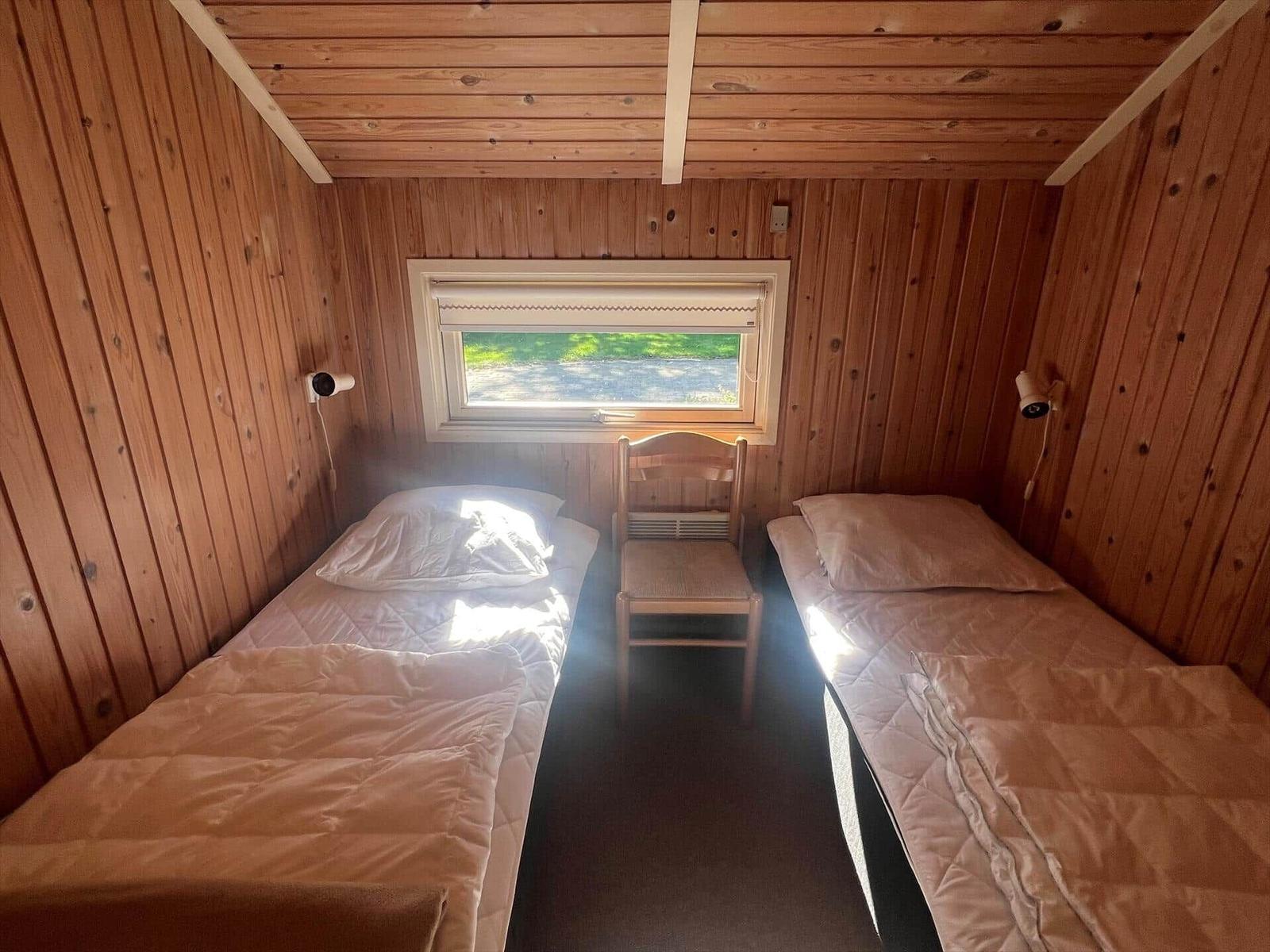 Zwei Einzelbetten in einem Holzraum mit Fenster und Stuhl.