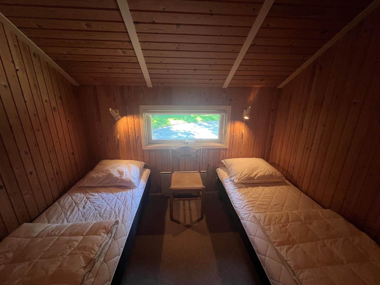 Zwei Betten in einem Holzraum mit Fenster und Stuhl