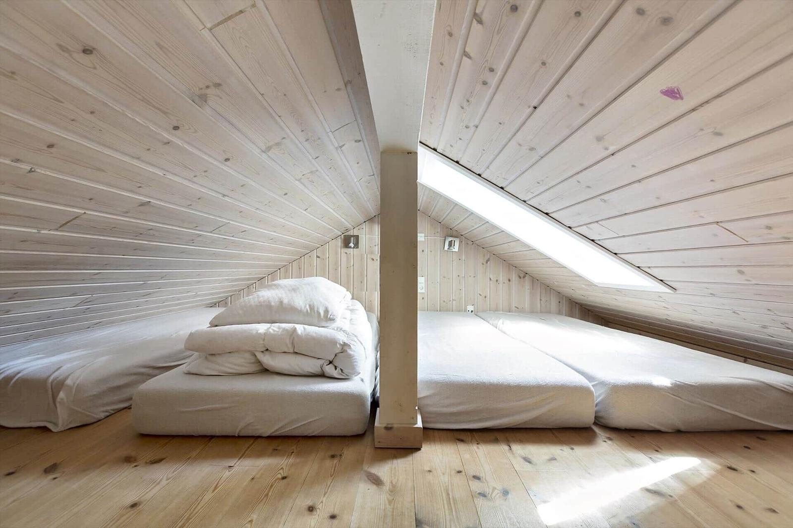Zwei Matratzen unter Dachschrägen mit Holzwänden und Boden. Ein Dachfenster sorgt für Licht.