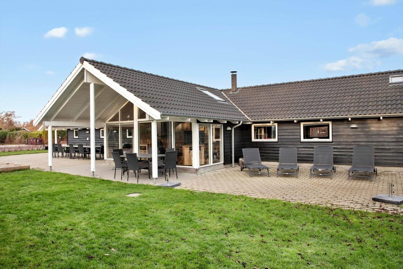 Moderne Ferienwohnung mit überdachtem Patio, Sitzgruppe und Liegestühlen auf Terrasse.