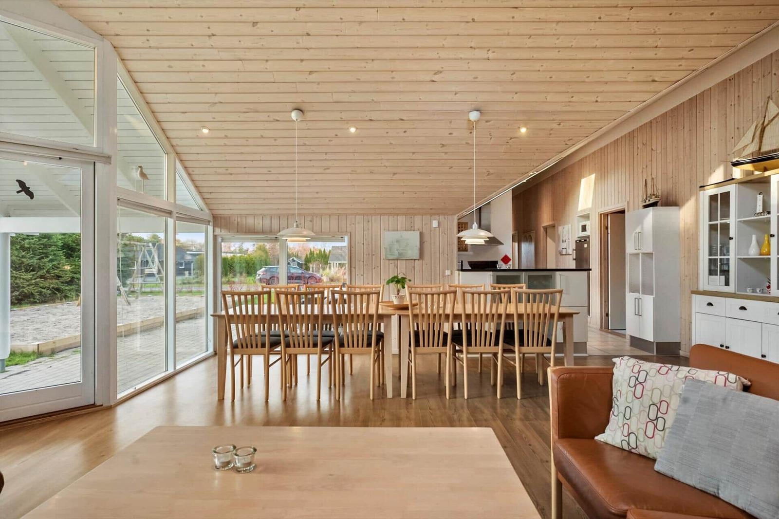 Großer Wohnraum mit Holzdecke, Esstisch und Sofa. Durchgehende Glasfront mit Blick auf den Außenbereich.