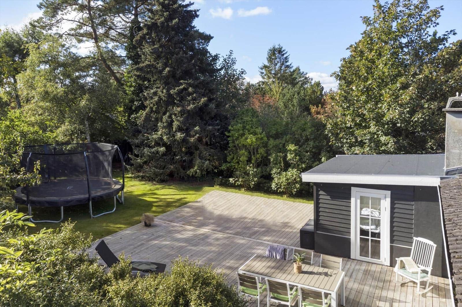 Hinterhof mit Terrasse, Tisch, Stühlen, Trampolin und Bäumen.