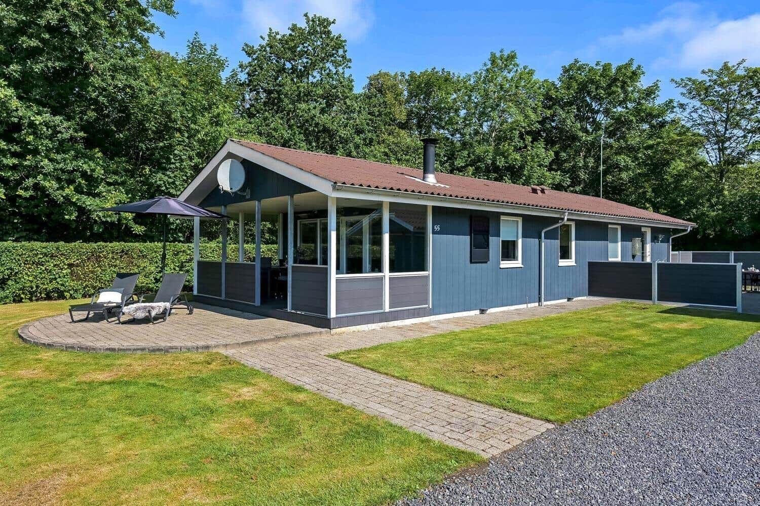 Ein graues Ferienhaus mit Terrasse, Liegestühlen und Grünfläche. Hinterhof mit Zaun.
