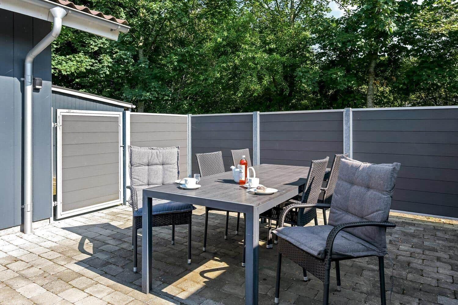 Terrasse mit Tisch und Stühlen, umgeben von grauen Wänden und Bäumen.