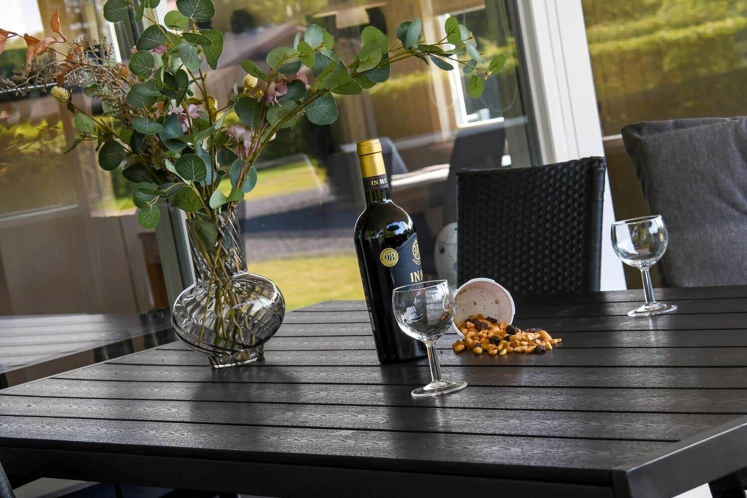 Ein Tisch mit Weinflasche, Gläsern und einer Vase mit Blumen.