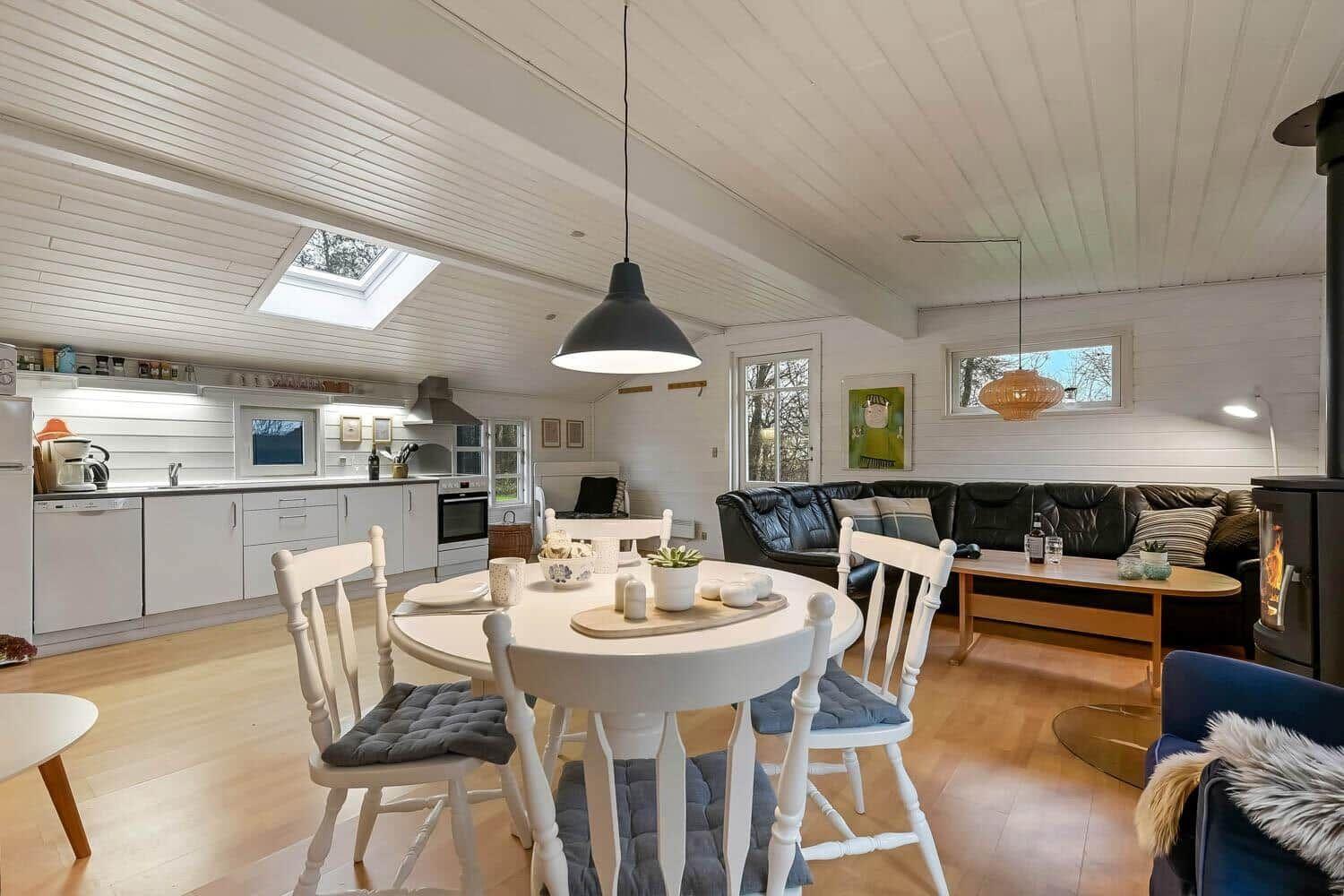 Wohnküche mit Esstisch, Sofa und Holzfußboden. Decke mit Dachfenster und Hängelampen.