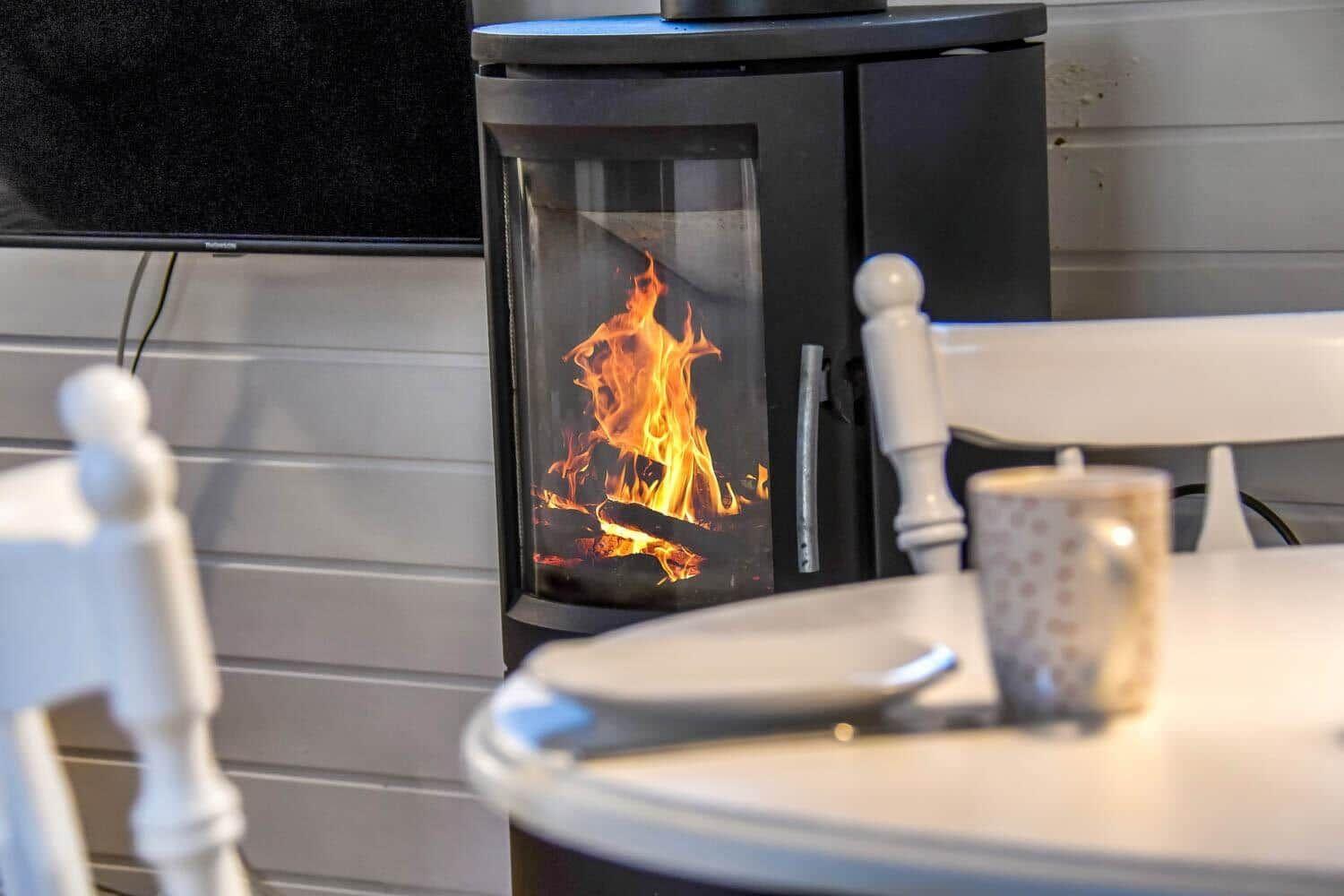 Ein Kaminofen mit brennendem Holz steht neben einem Tisch mit Stühlen.
