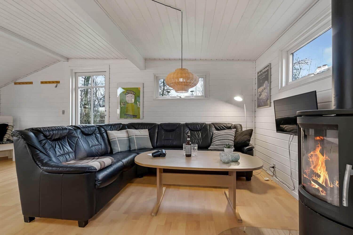 Wohnzimmer mit schwarzer Ledercouch, Holztisch und Kaminofen. Weiße Wände und Holzboden.