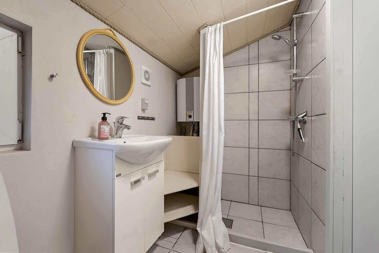 Bad mit Dusche, Waschbecken und Spiegel. Duschbereich mit Fliesen und Vorhang.