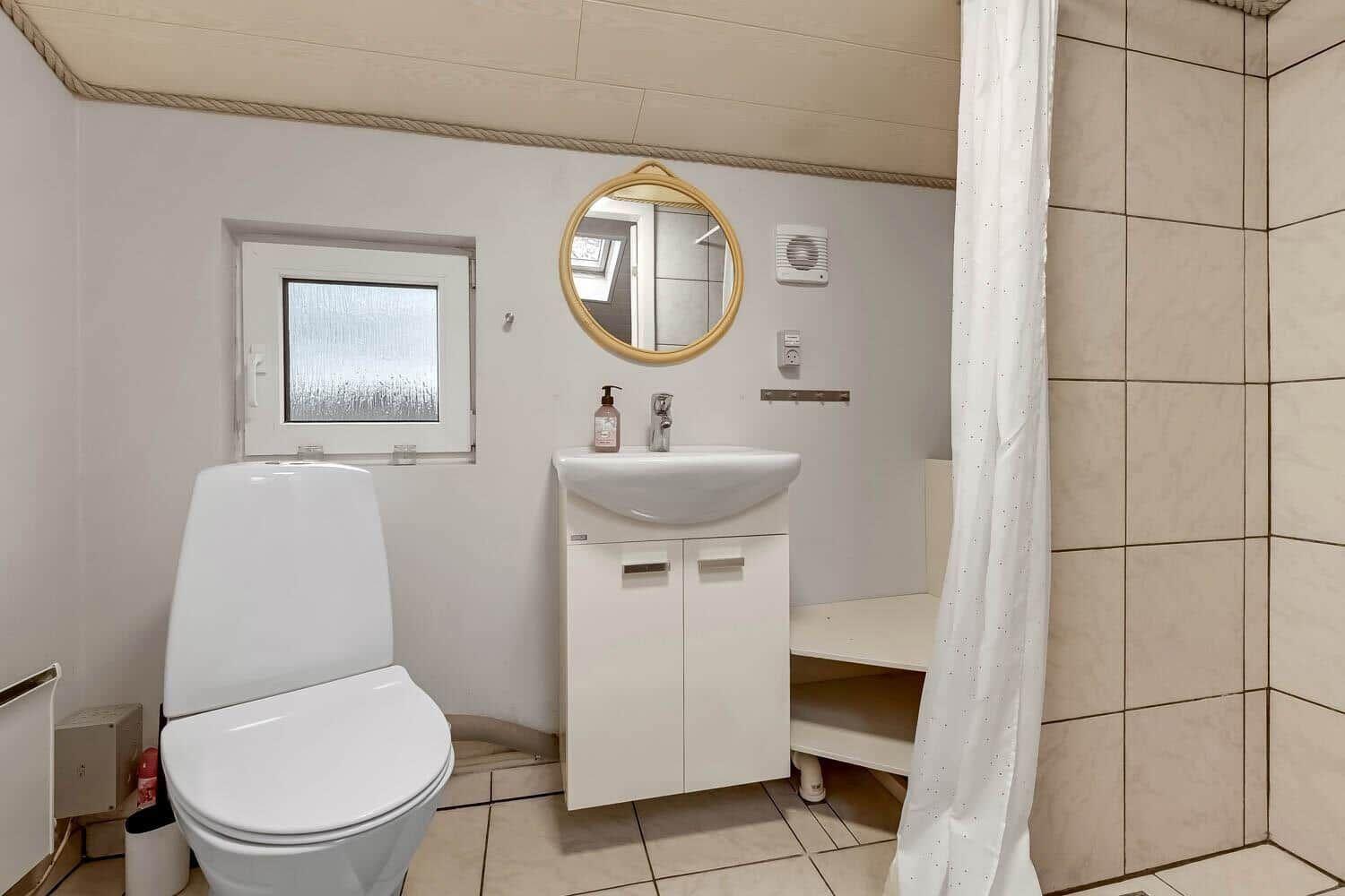Badezimmer mit Toilette, Waschbecken und Dusche mit Vorhang.