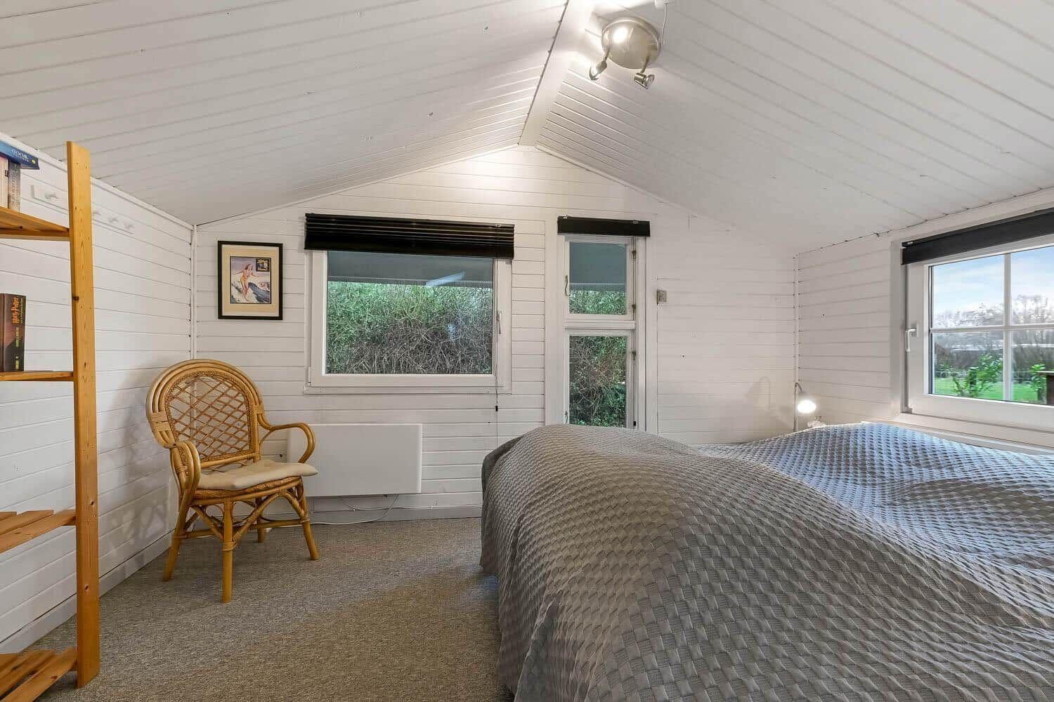Schlafzimmer mit Bett, Stuhl und Fenstern. Weiße Wände und Decke.