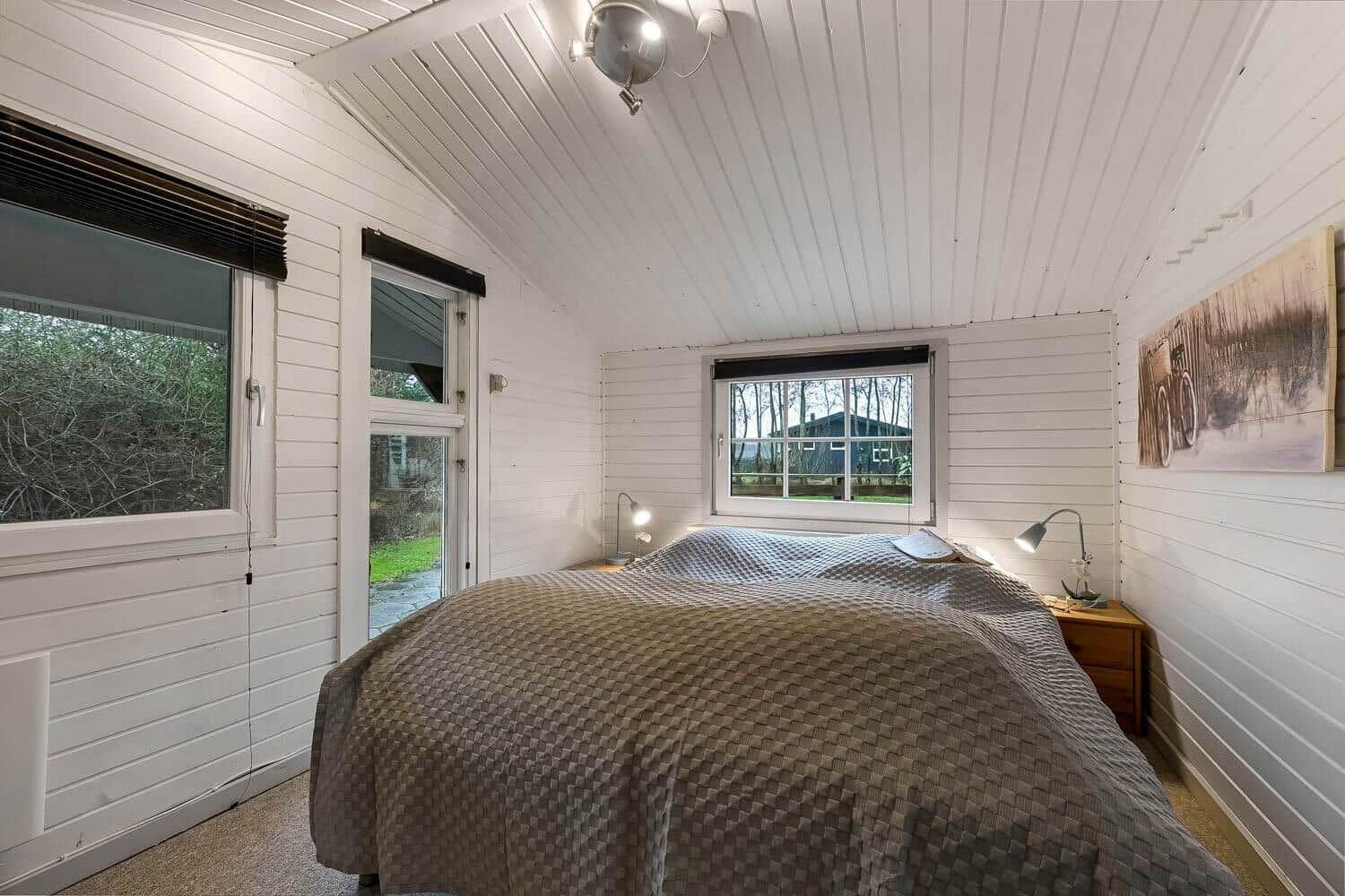 Schlafzimmer mit Bett, Fenstern und Wandbild. Decke mit Holzverkleidung.