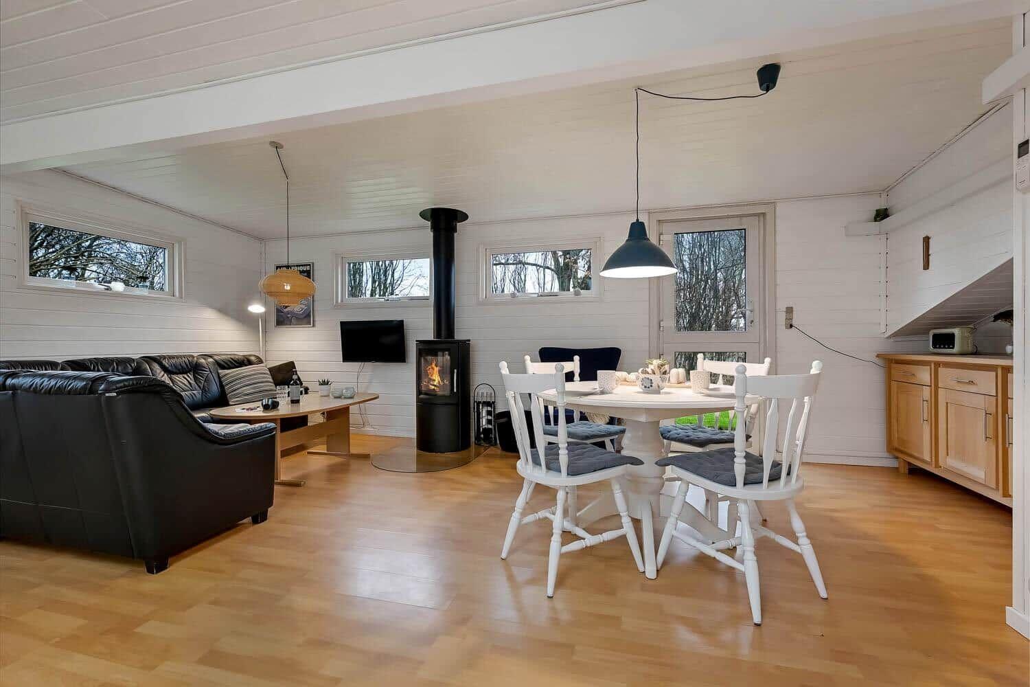 Wohn- und Essbereich mit Kamin, Esstisch und Sofa. Holzboden und weiße Wände.
