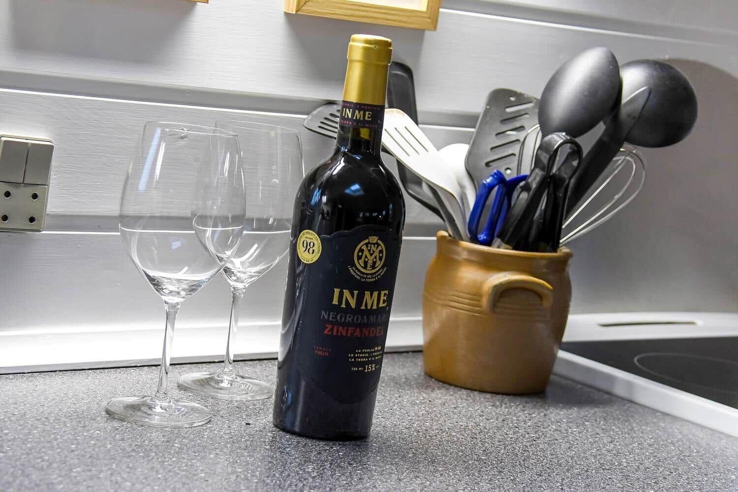 Eine Flasche Wein mit zwei Gläsern auf Küchenarbeitsplatte neben Küchenutensilien.