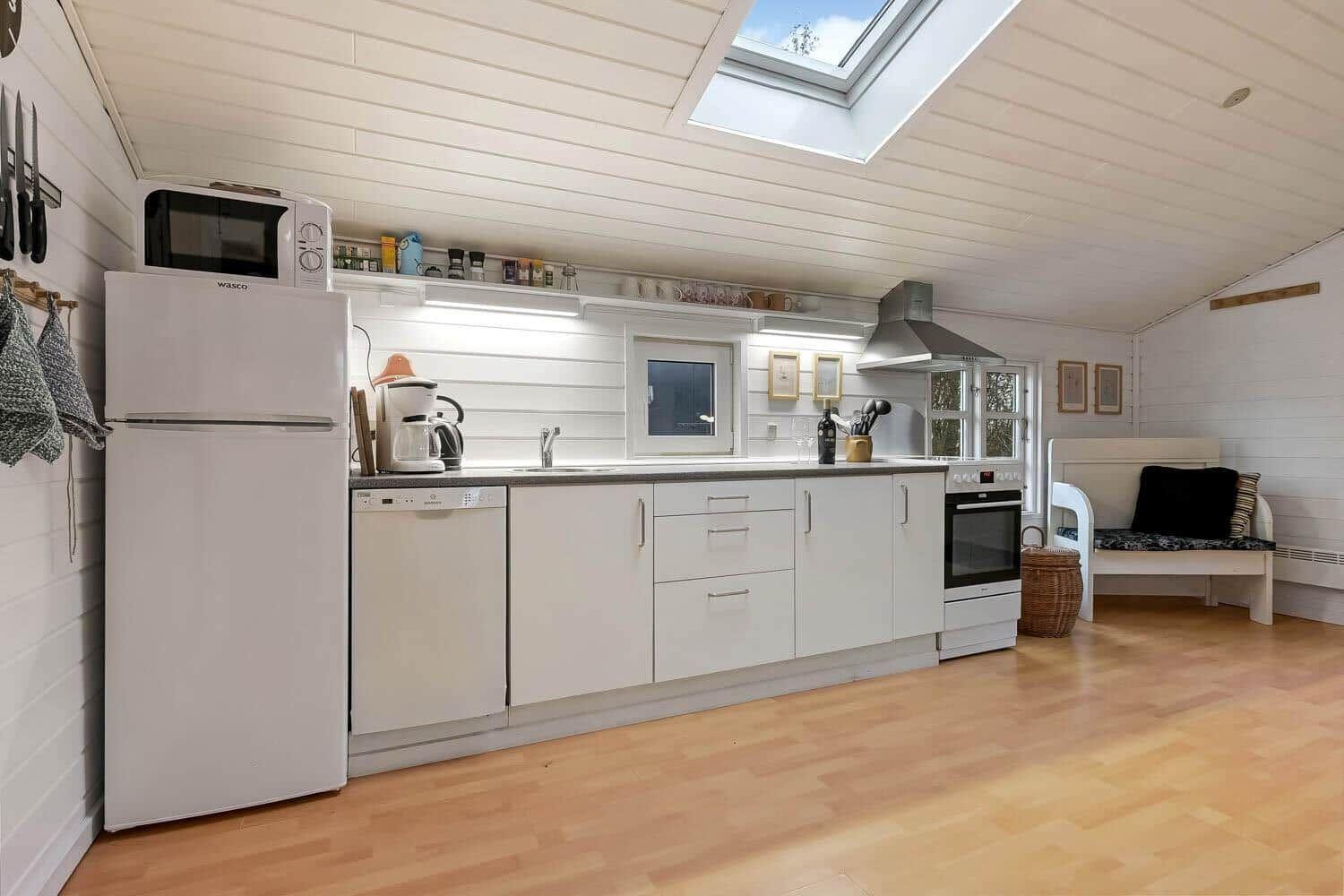 Küche mit weißer Einbauküche, Kühlschrank, Spülmaschine und Fenster.