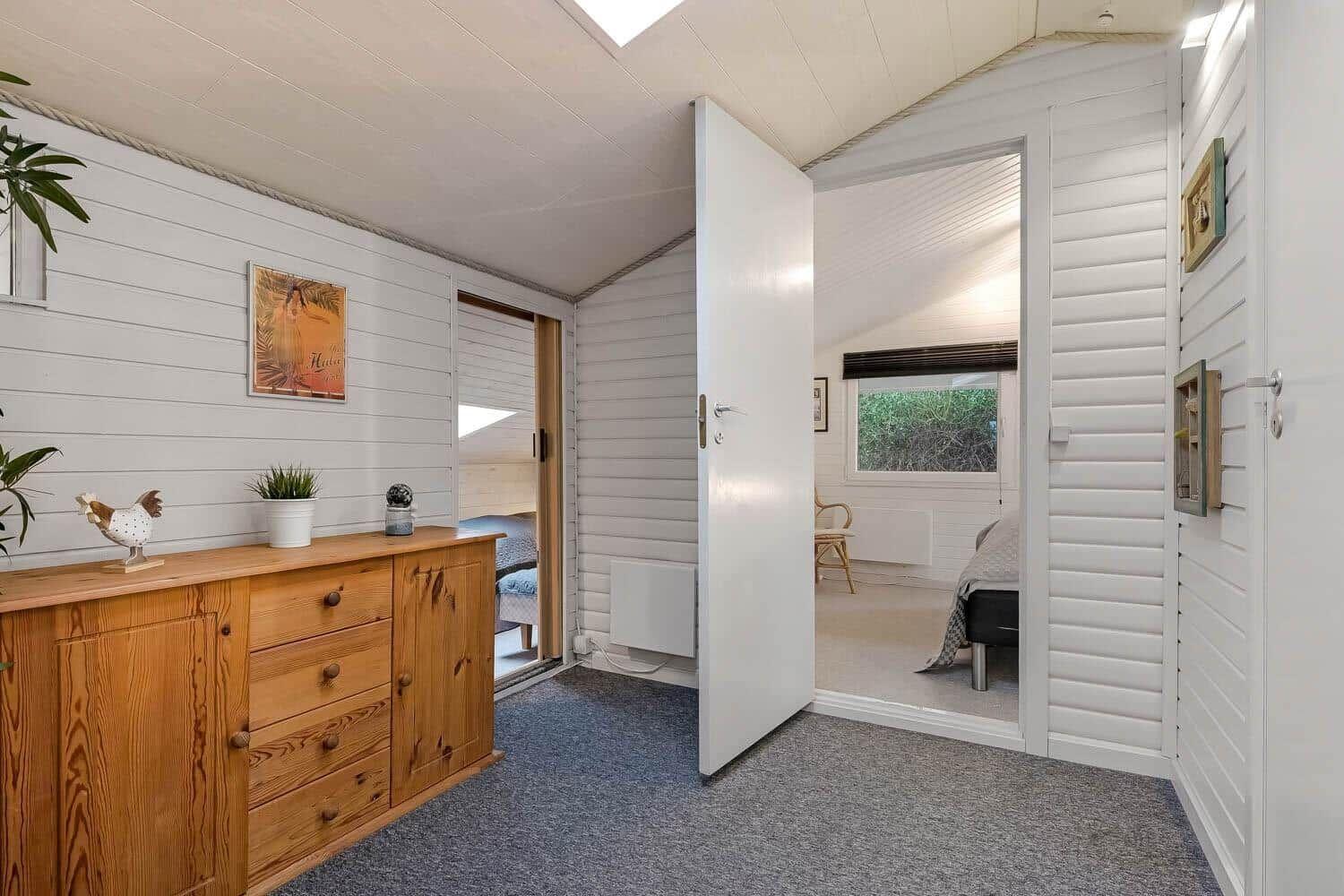 Wohnraum mit Holzschrank und Blick in Schlafzimmer mit Bett und Fenster.