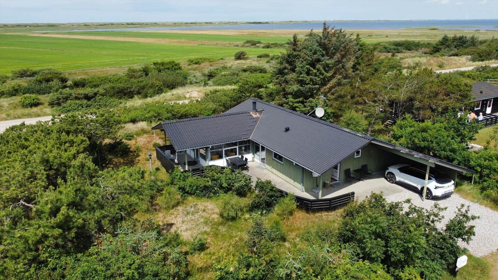 Einhaus mit Terrasse und Carport, umgeben von Grünflächen und Wasser.