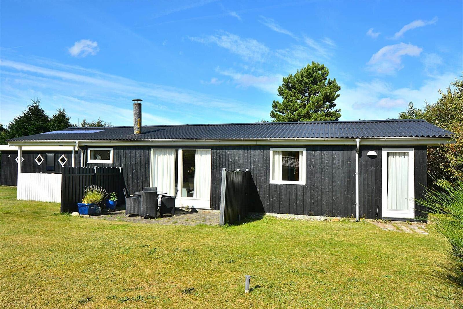 Ein schwarz verputztes Ferienhaus mit weiß gerahmten Fenstern und einer Terrasse im Garten.