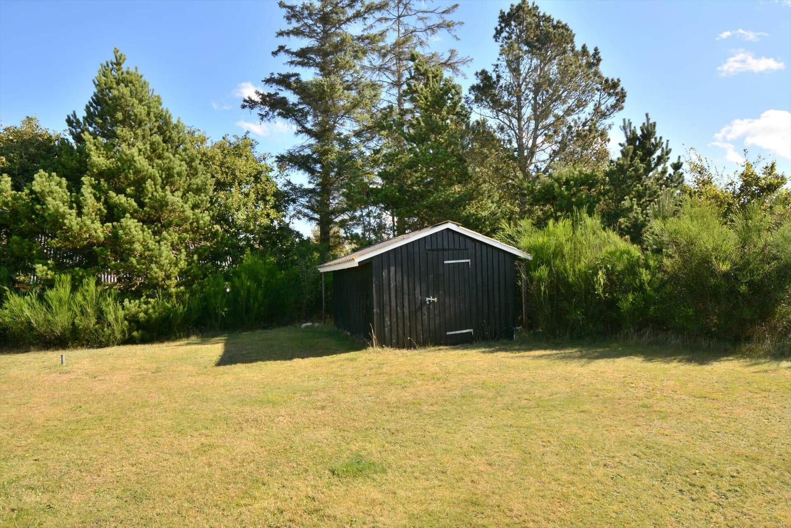 Schwarze Hütte im Grünen mit Grasfläche und Bäumen im Hintergrund.
