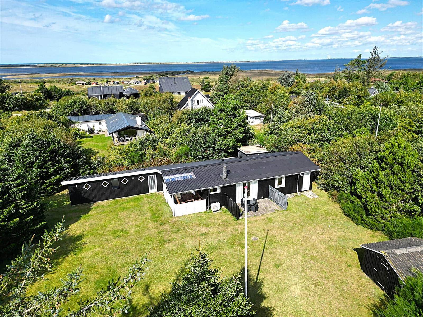 Schwarzes Haus mit Garten, umgeben von Bäumen und Blick auf das Meer.