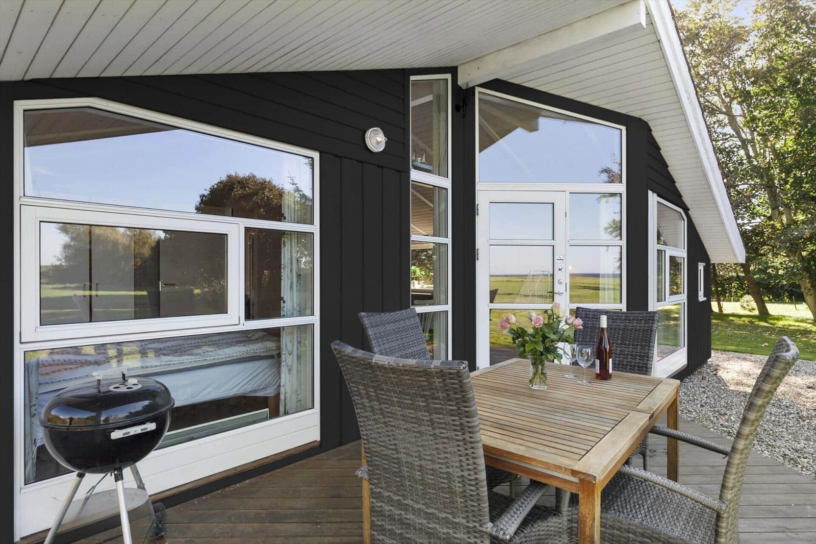 Terrasse mit Tisch, Stühlen und Grill. Schwarze Fassade und große Fenster.
