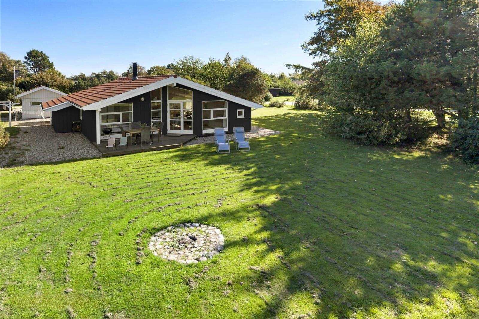 Ein Haus mit Terrasse, Garten und Liegestühlen unter Bäumen.