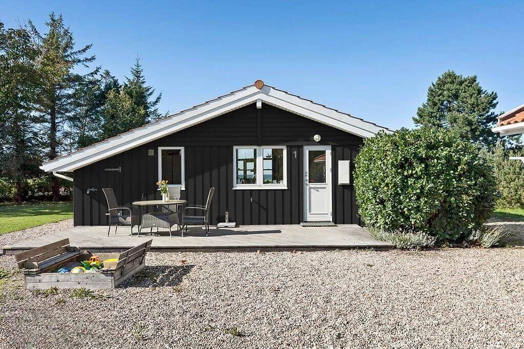 Schwarzes Holzhaus mit weißem Dach, Terrasse und Garten. Gartenmöbel und Spielzeugkiste sichtbar.