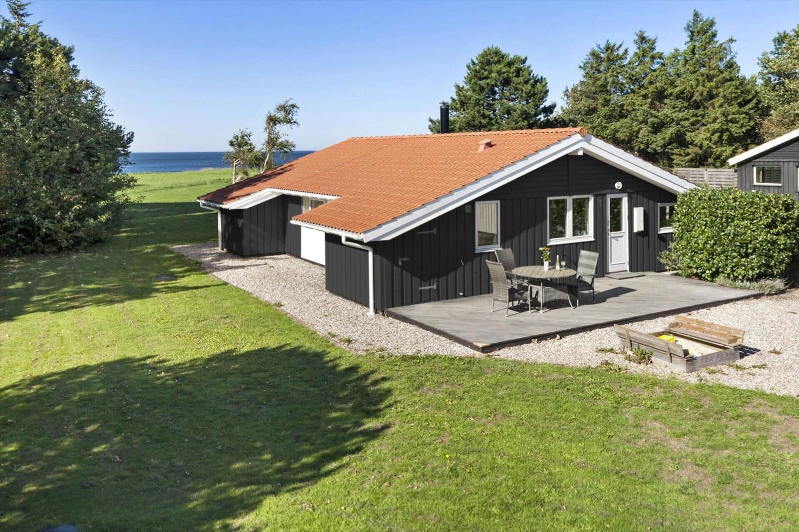 Schwarzes Haus mit Terrasse und Garten. Blick auf das Meer. Holztisch mit Stühlen.