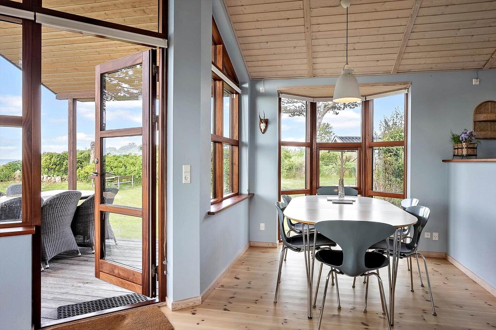 Esszimmer mit Tisch, Stühlen und Blick auf Garten. Holzdecke und Boden.