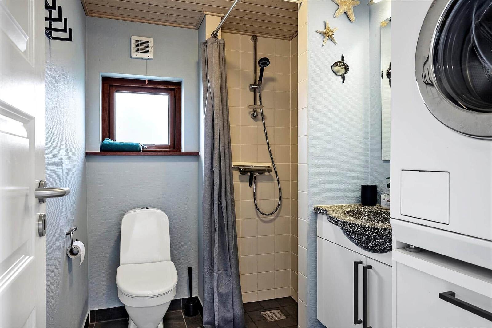 Badezimmer mit Dusche, Toilette und Waschmaschine. Fenster mit Handtuch.