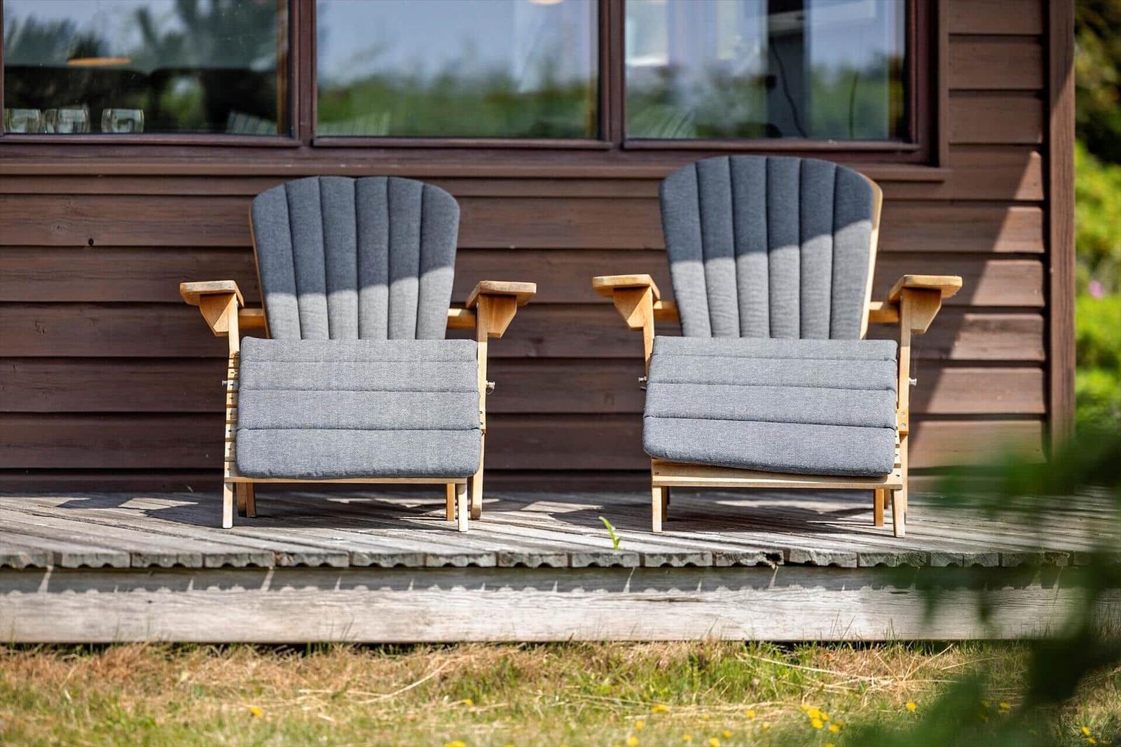 Zwei graue Sessel mit Holzrahmen stehen auf einer Terrasse vor einem Holzhaus.