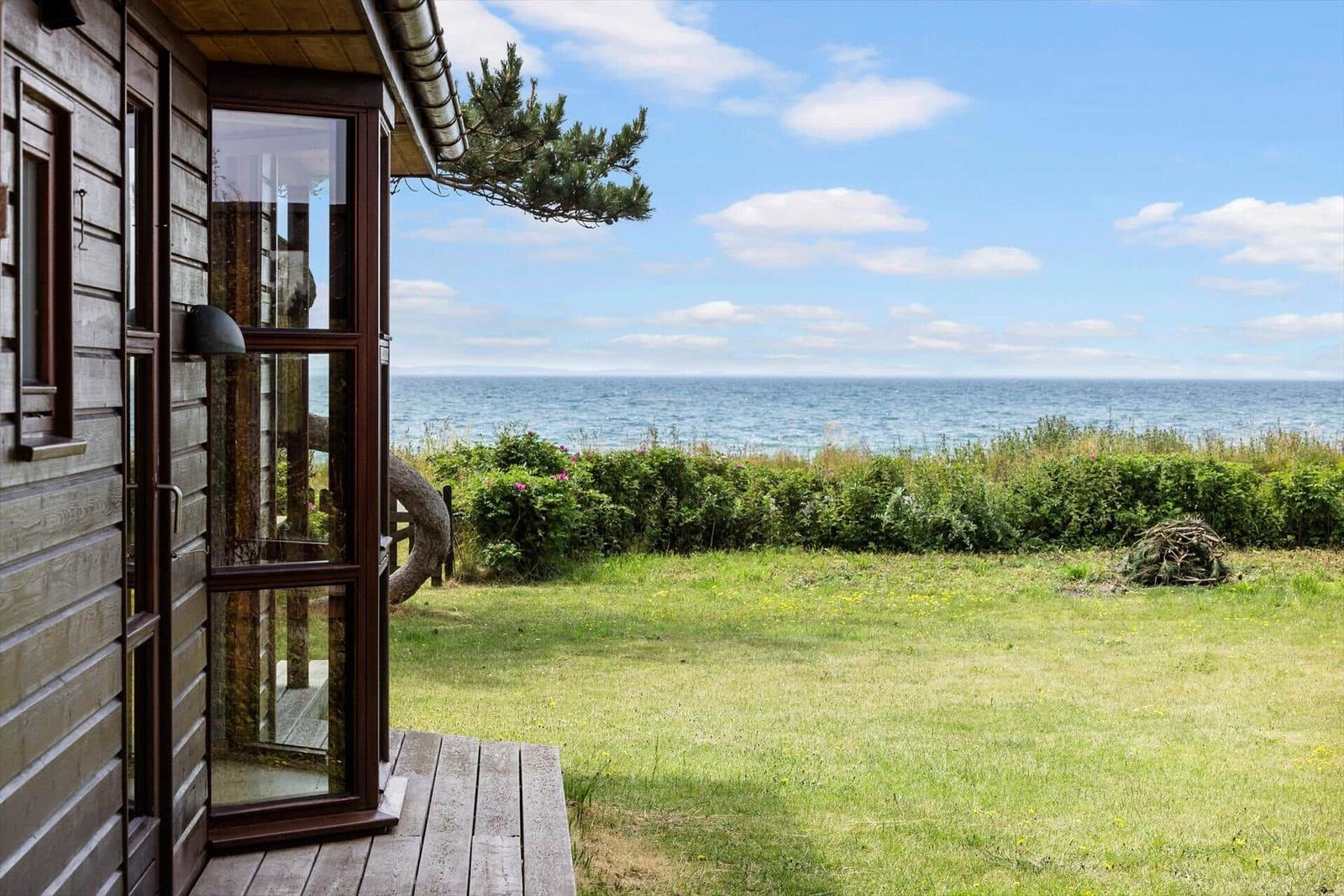 Von der Terrasse aus blickt man auf das Meer und einen grünen Garten.