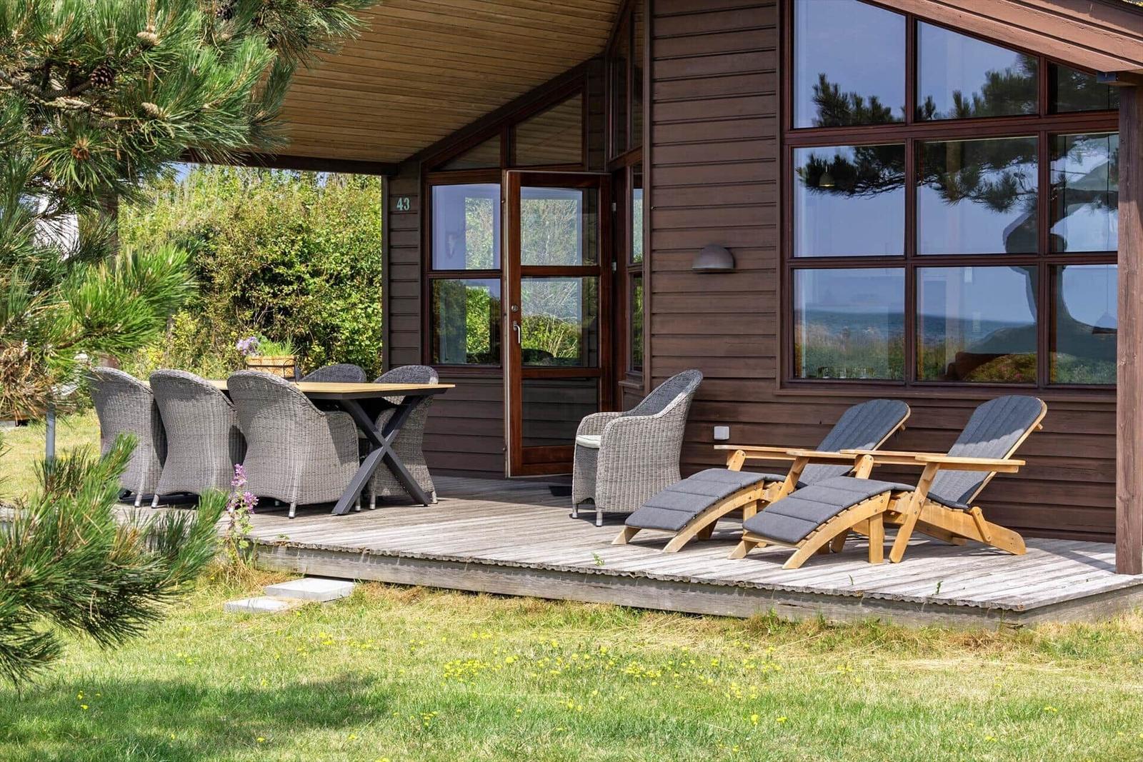 Terrasse mit Tisch, Stühlen und Liegen vor einem Holzhaus mit großen Fenstern.