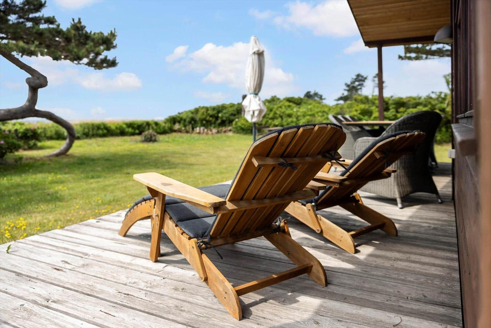 Zwei hölzerne Liegestühle mit Kissen auf einer Terrasse mit Blick auf einen grünen Garten.