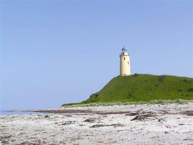 Leuchtturm auf grüner Anhöhe über Strand und Meer