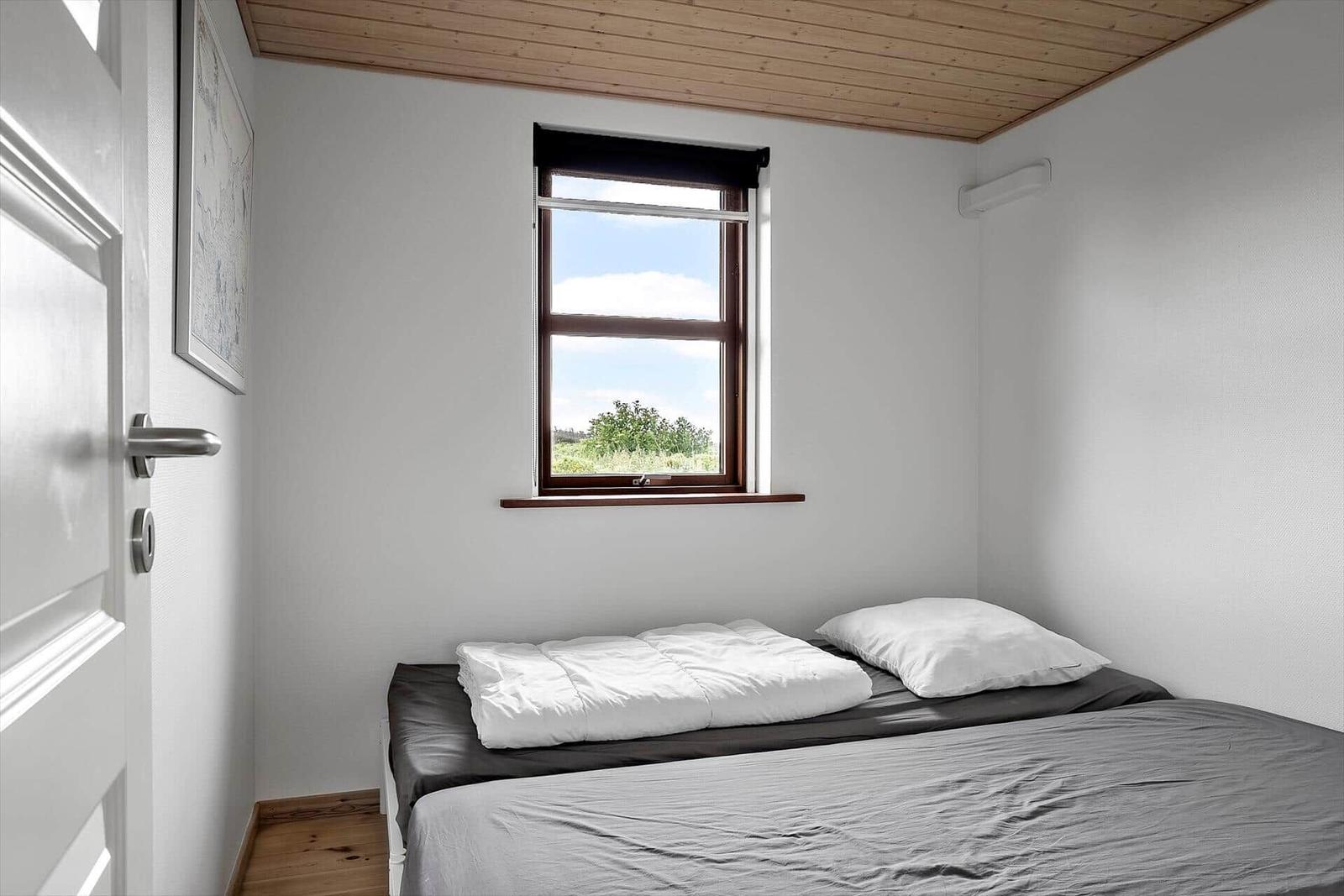Schlafzimmer mit Bett, Fenster und Holzdecke.