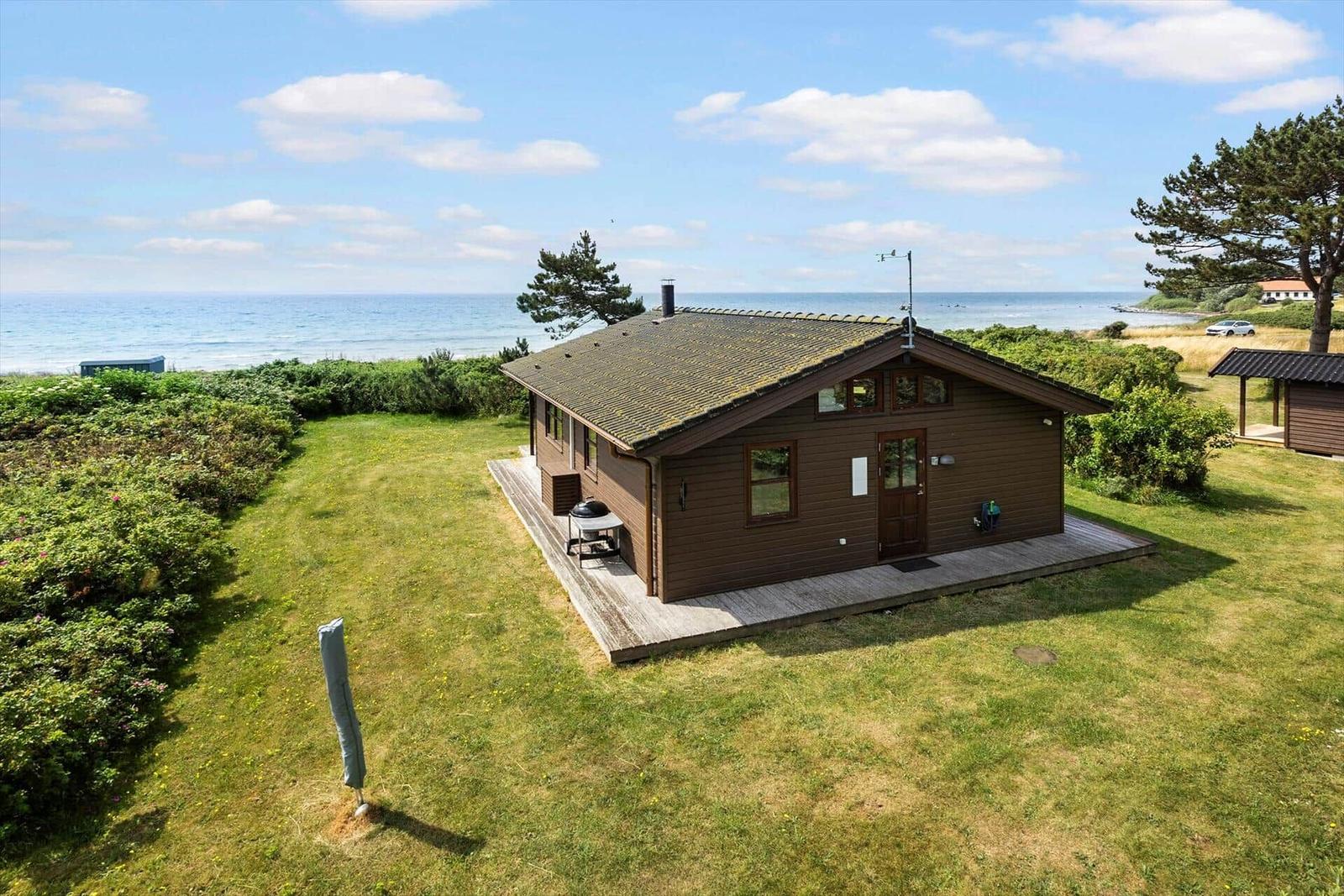 Holzhütte mit Terrasse, Garten und Meerblick. Grill und Sonnenschirm vorhanden.