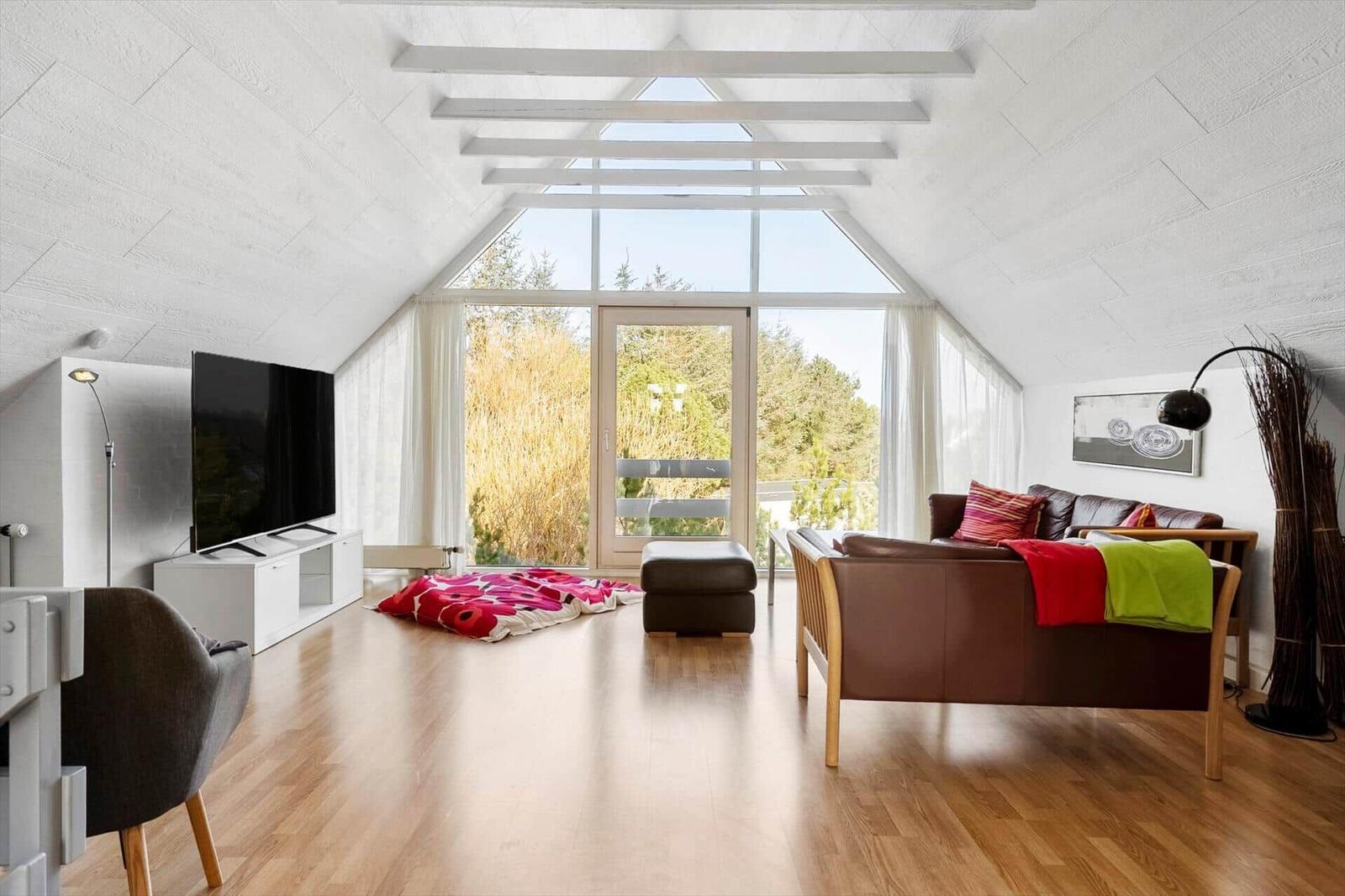 Living room with wooden floor, sofa, TV, and large window with view of nature.