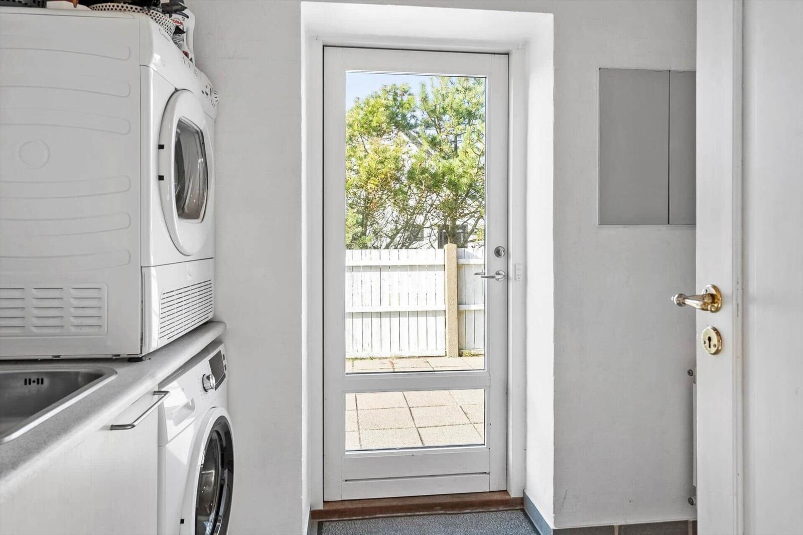 Washing machine and dryer next to a door with view of a paved outdoor area.
